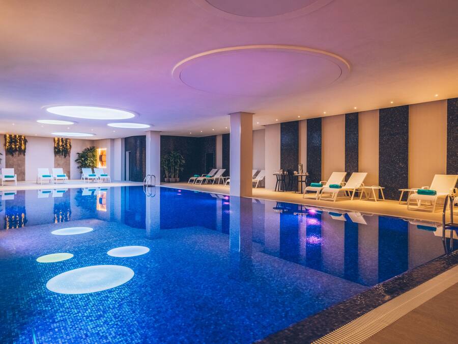Una piscina interior con sillones de descanso y un diseño moderno en el techo.