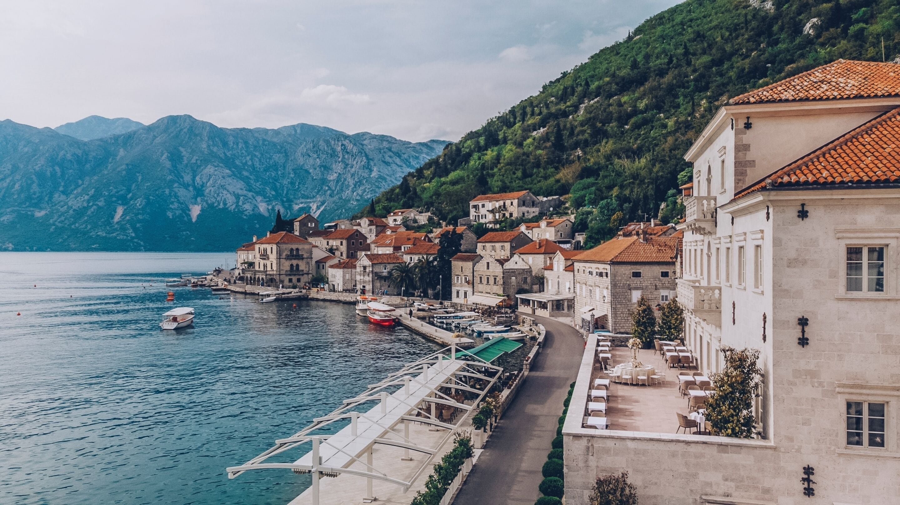 A coastal town with buildings along the waterfront, a pier, and mountains in the background.