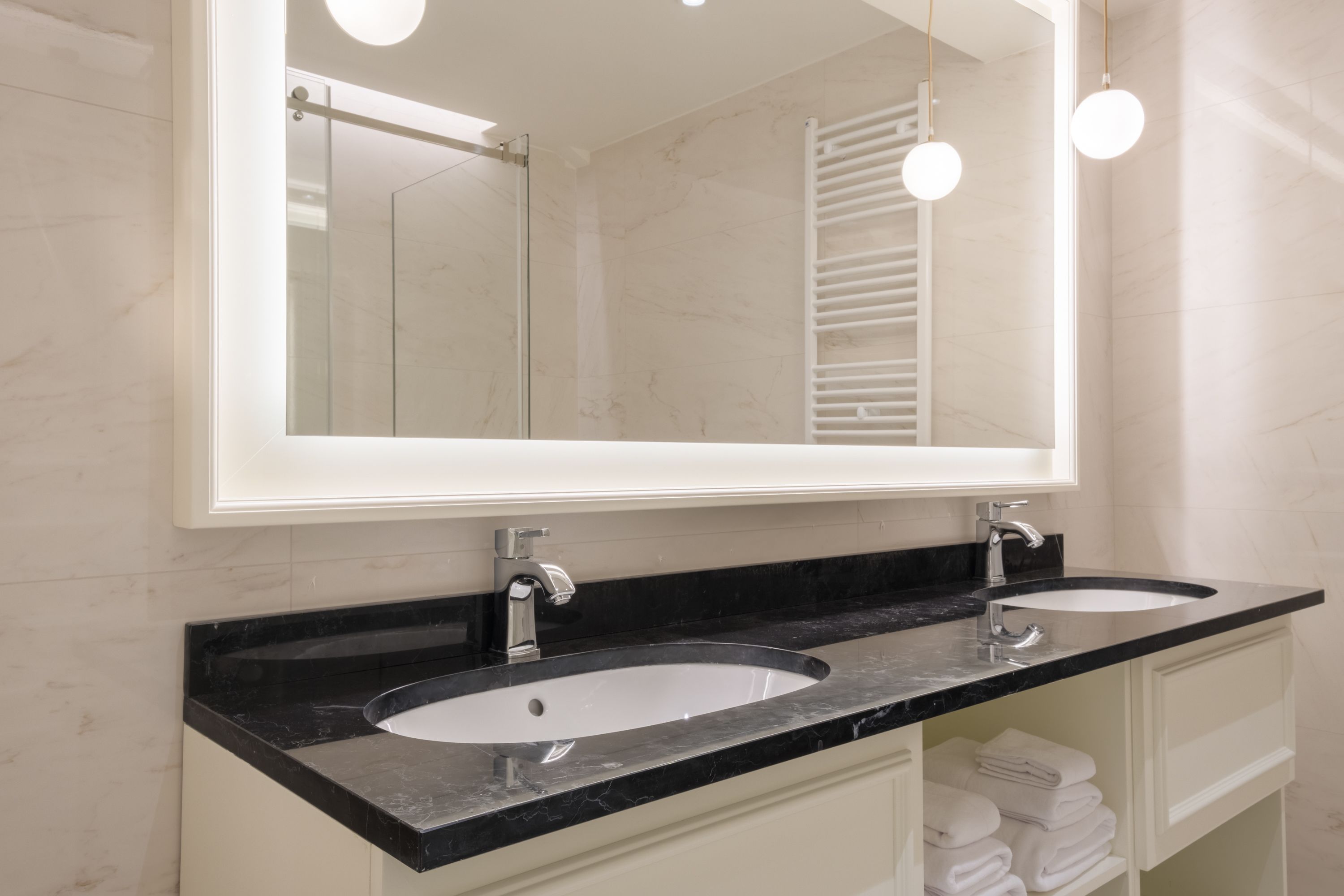 Un baño con dos lavamanos, un espejo grande y un perchero para toallas.