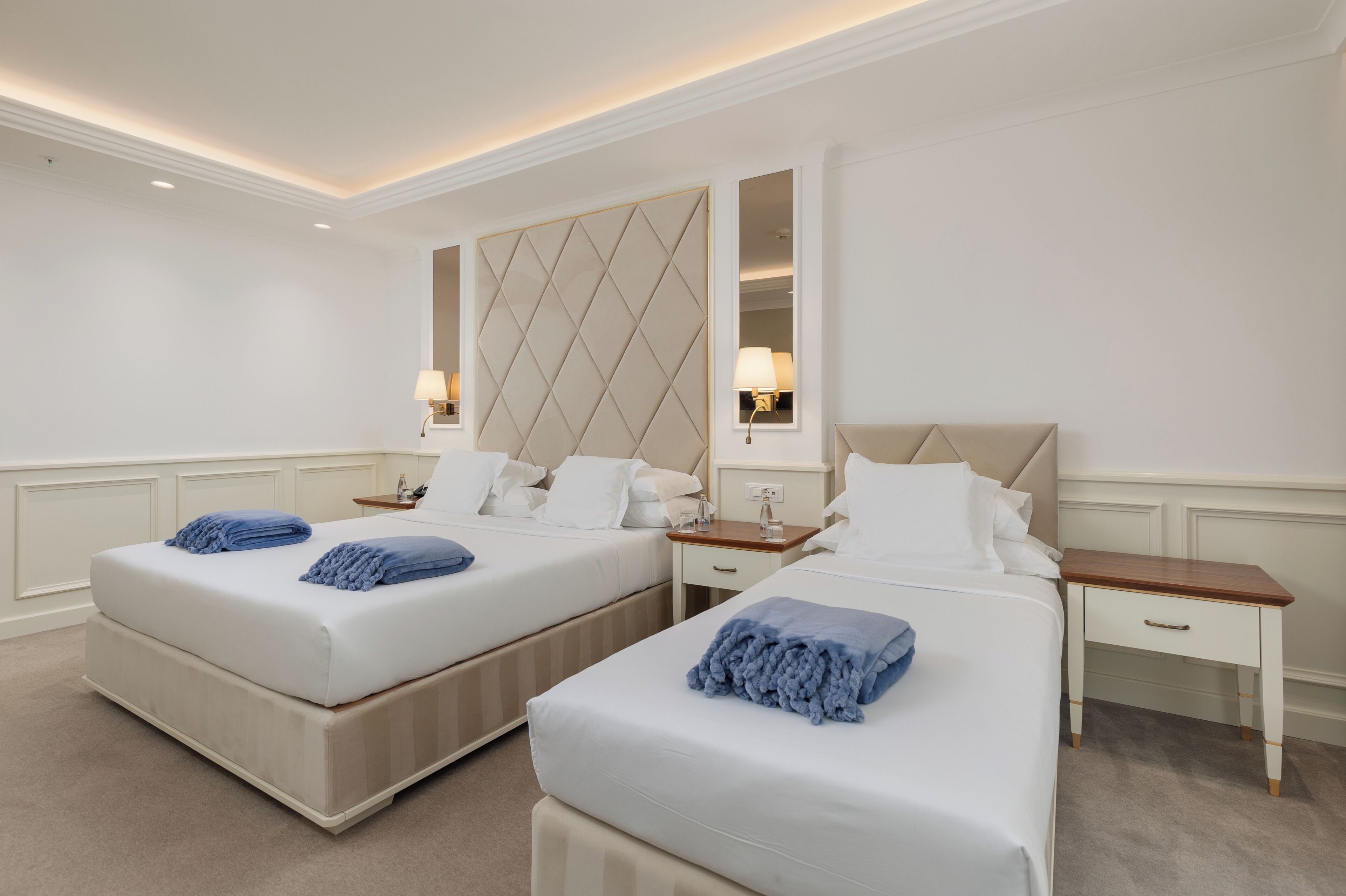 A hotel room with two beds, each with a headboard, bedside tables, and lamps.