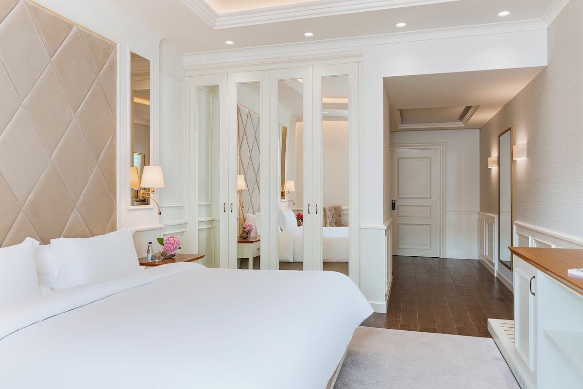 A hotel room with a large bed, a wardrobe with mirrored doors, and a small table with a lamp.