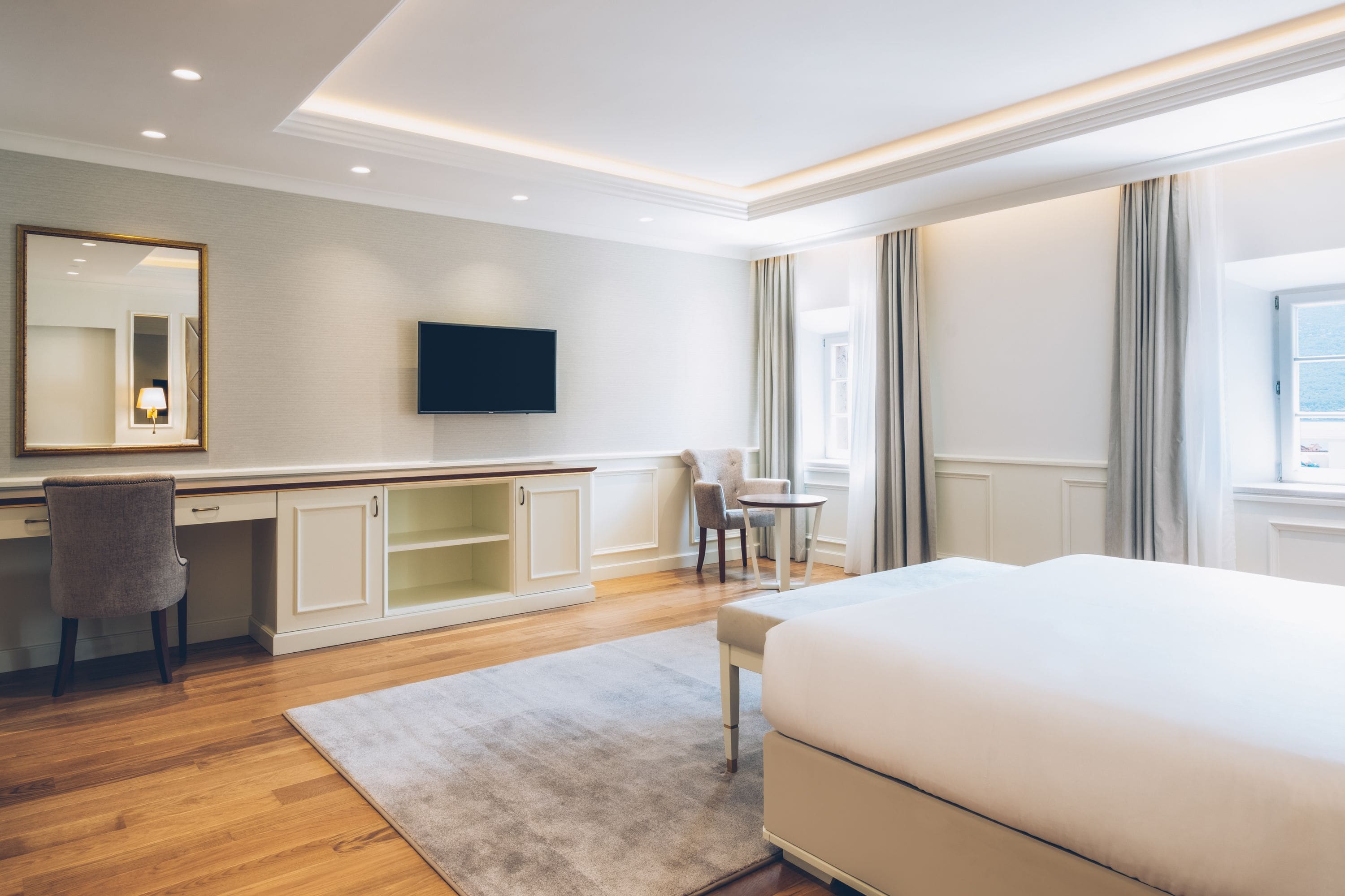 A hotel room with a large bed, a desk with a chair, a television, and a window with curtains.