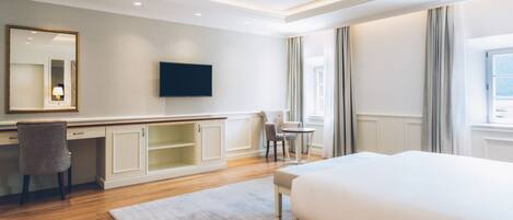 A hotel room with a large bed, a desk with a chair, a television, and a window with curtains.