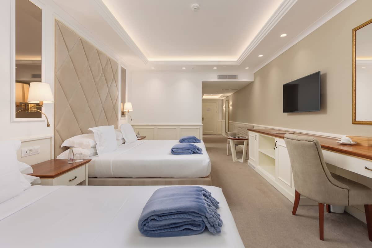 A hotel room with two beds, a desk, a chair, a TV, and a minibar.