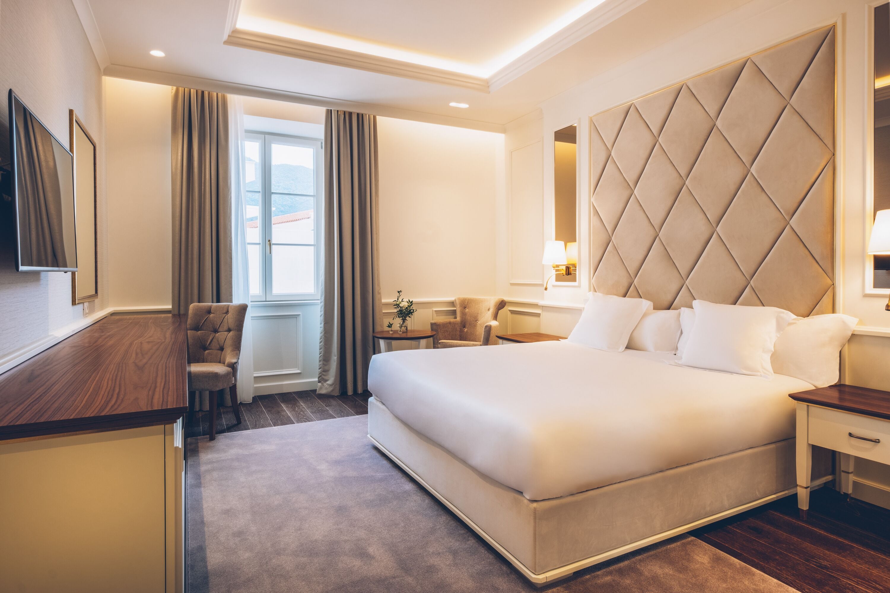 Habitación de hotel con una cama grande, un escritorio, una silla, un televisor y una ventana con cortinas.