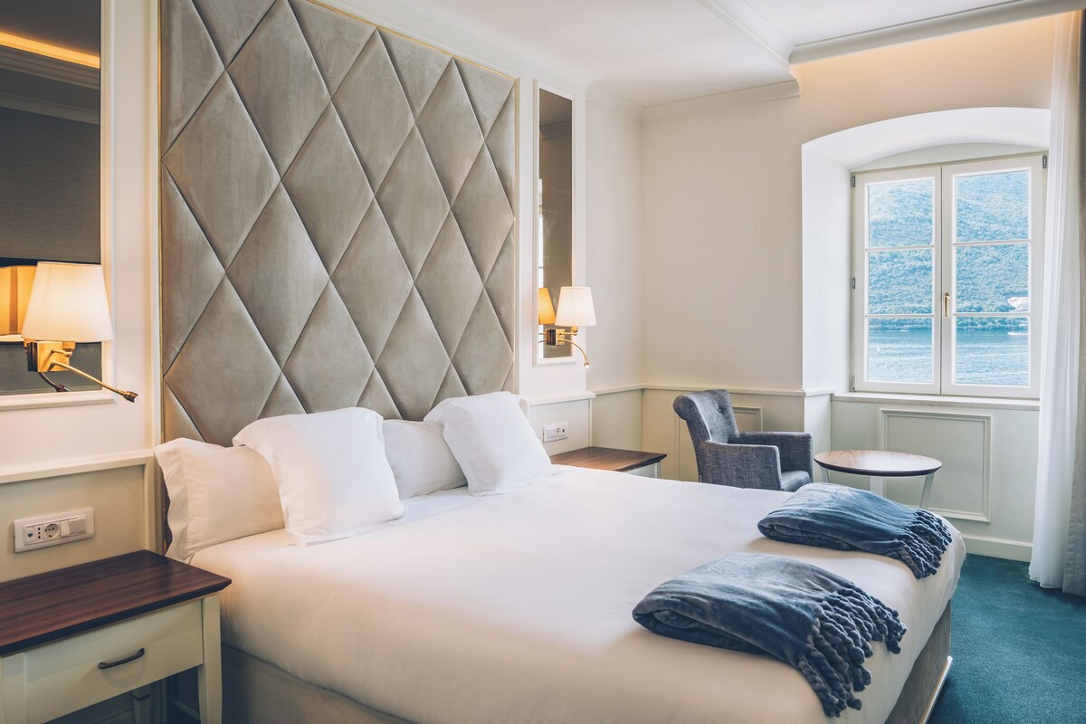 Una habitación de hotel con una cama grande, un escritorio, una silla, una mesita y una ventana con vista al mar.