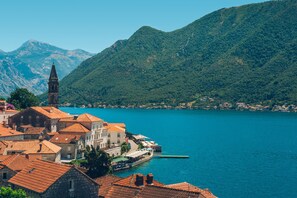 A coastal town with historic buildings, a prominent church tower, and a clear view of the surrounding mountains and lake. - Heritage Grand Perast (Perast)