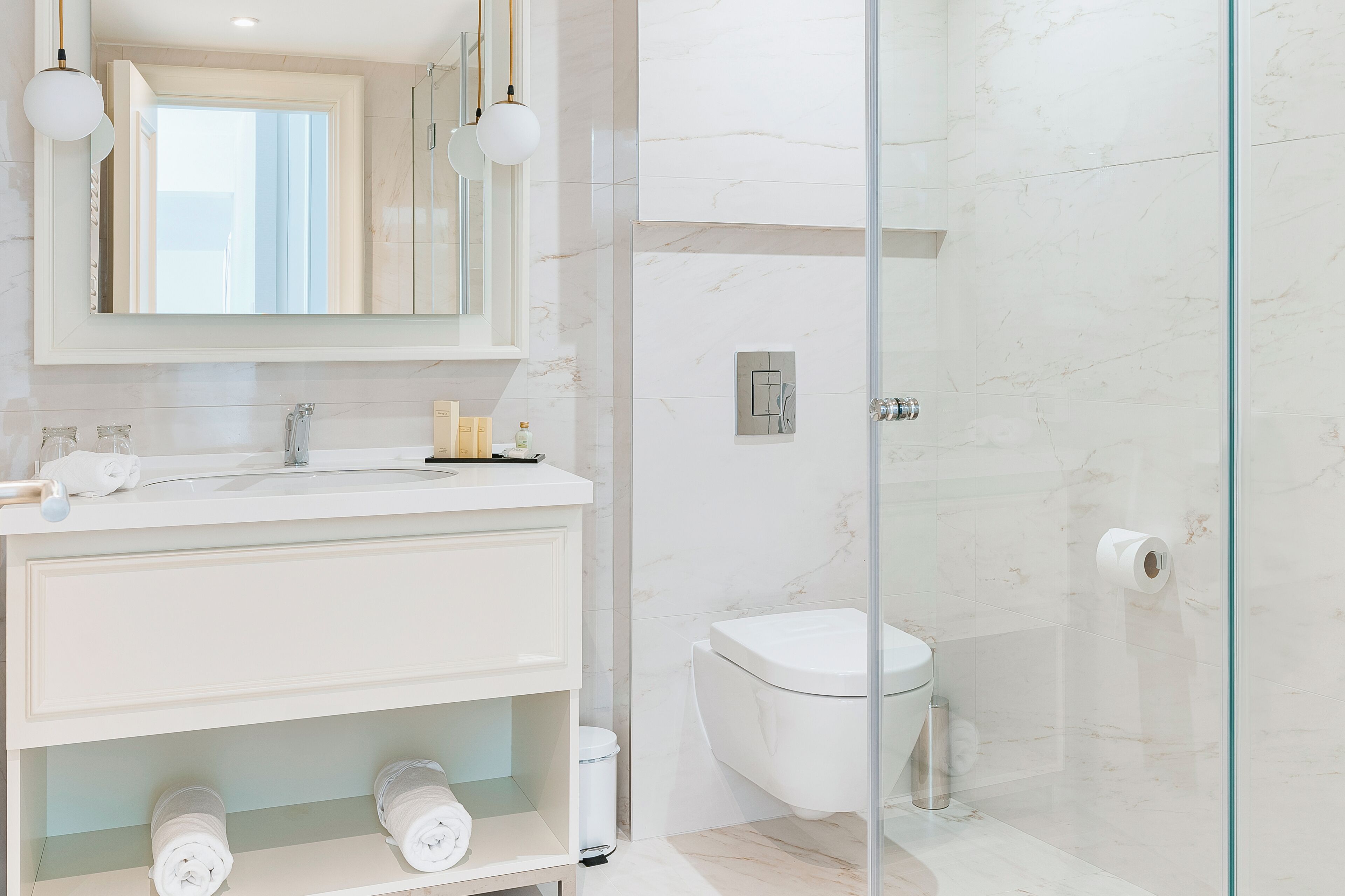 Un baño moderno con cabina de ducha de vidrio, inodoro blanco y tocador con espejo y toallero.