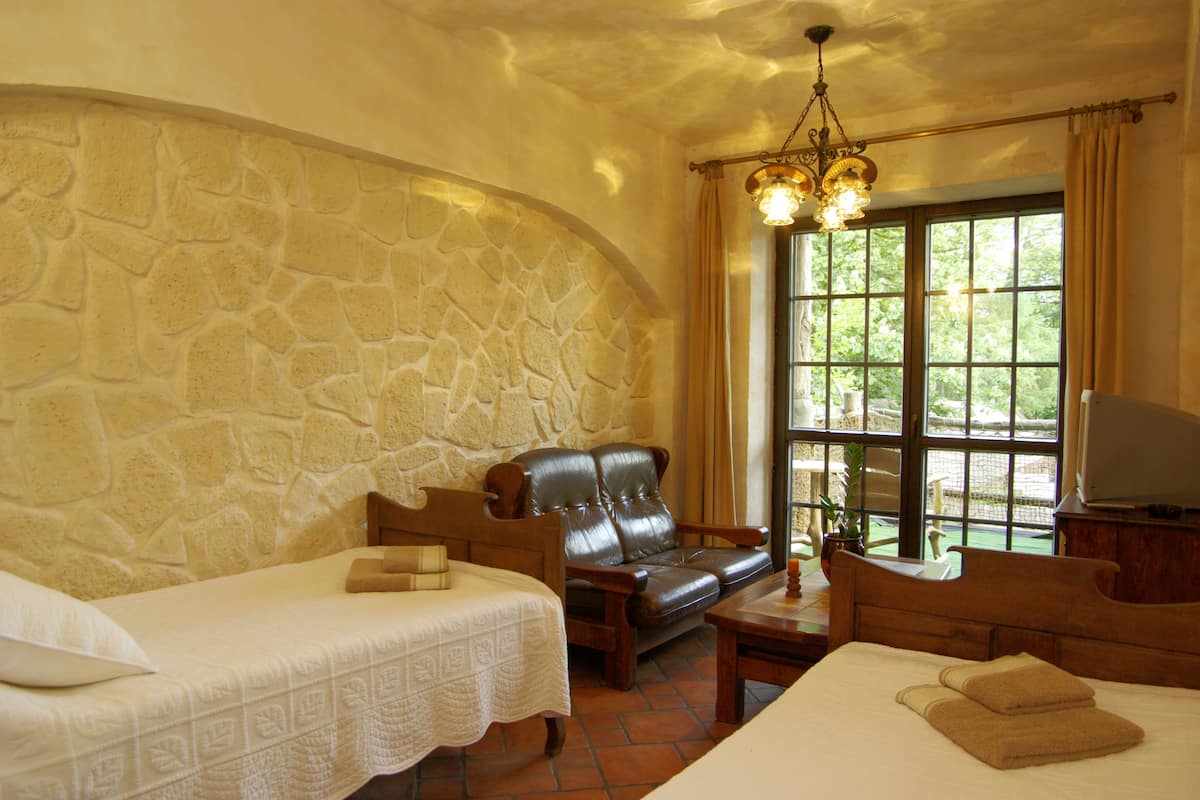 A room with a stone wall, a bed, a sofa, a TV, and a window with curtains.