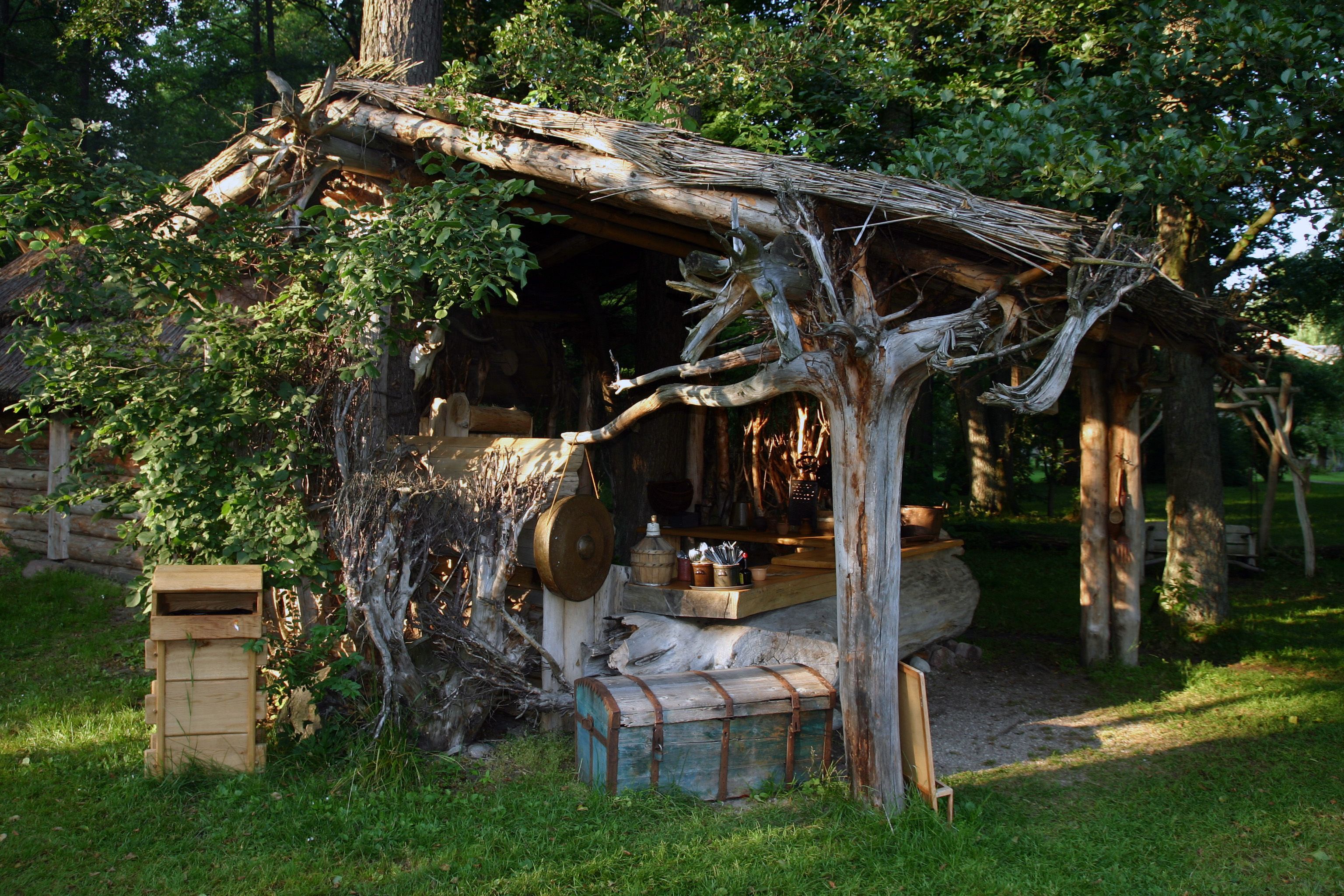 A rustic wooden structure with a thatched roof, surrounded by greenery.