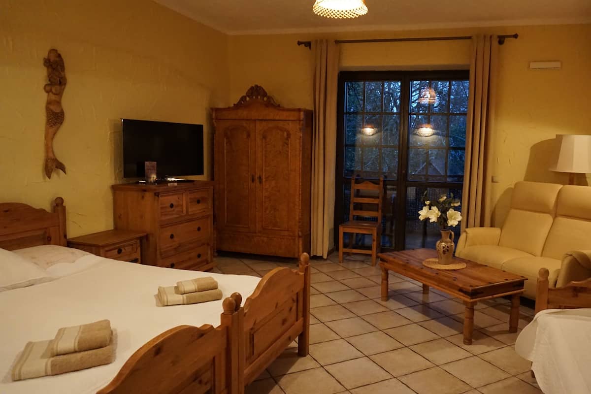 A hotel room with a bed, a wooden desk, a chair, a television, a wardrobe, and a window with curtains.