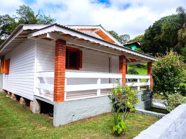 Una casa de madera de dos pisos con fachada blanca y detalles de ladrillo rojo, que cuenta con un porche y un pequeño jardín.