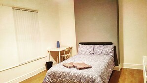 A small, neatly arranged bedroom with a bed, a chair, and a small table.