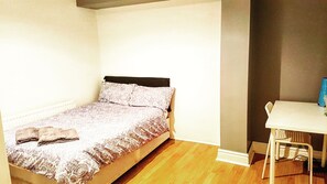 A small, single-bed room with a wooden floor, a white desk, and a chair. - Molyneux Place (Liverpool)
