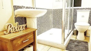 A bathroom with a wooden vanity, a sink, a toilet, and a shower area. - Molyneux Place (Liverpool)