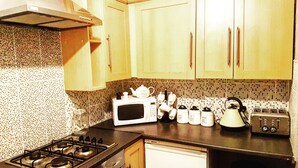 A kitchen with wooden cabinets, a gas stove, a microwave, a toaster, and a kettle.