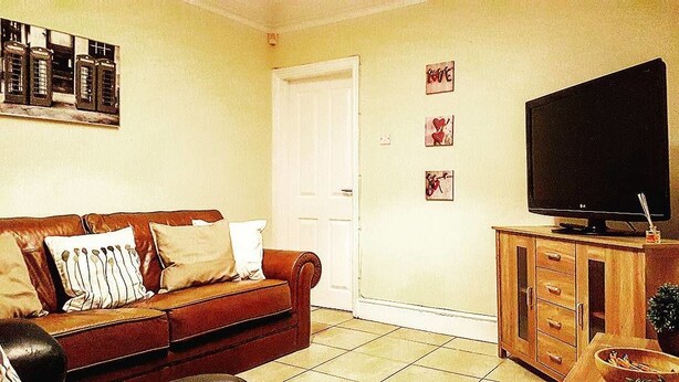 A living room with a brown leather sofa, a television on a wooden cabinet, and a door in the background.