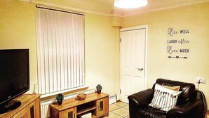 A living room with a television, a wooden cabinet, a black leather sofa, a white door, and a wall with motivational text.