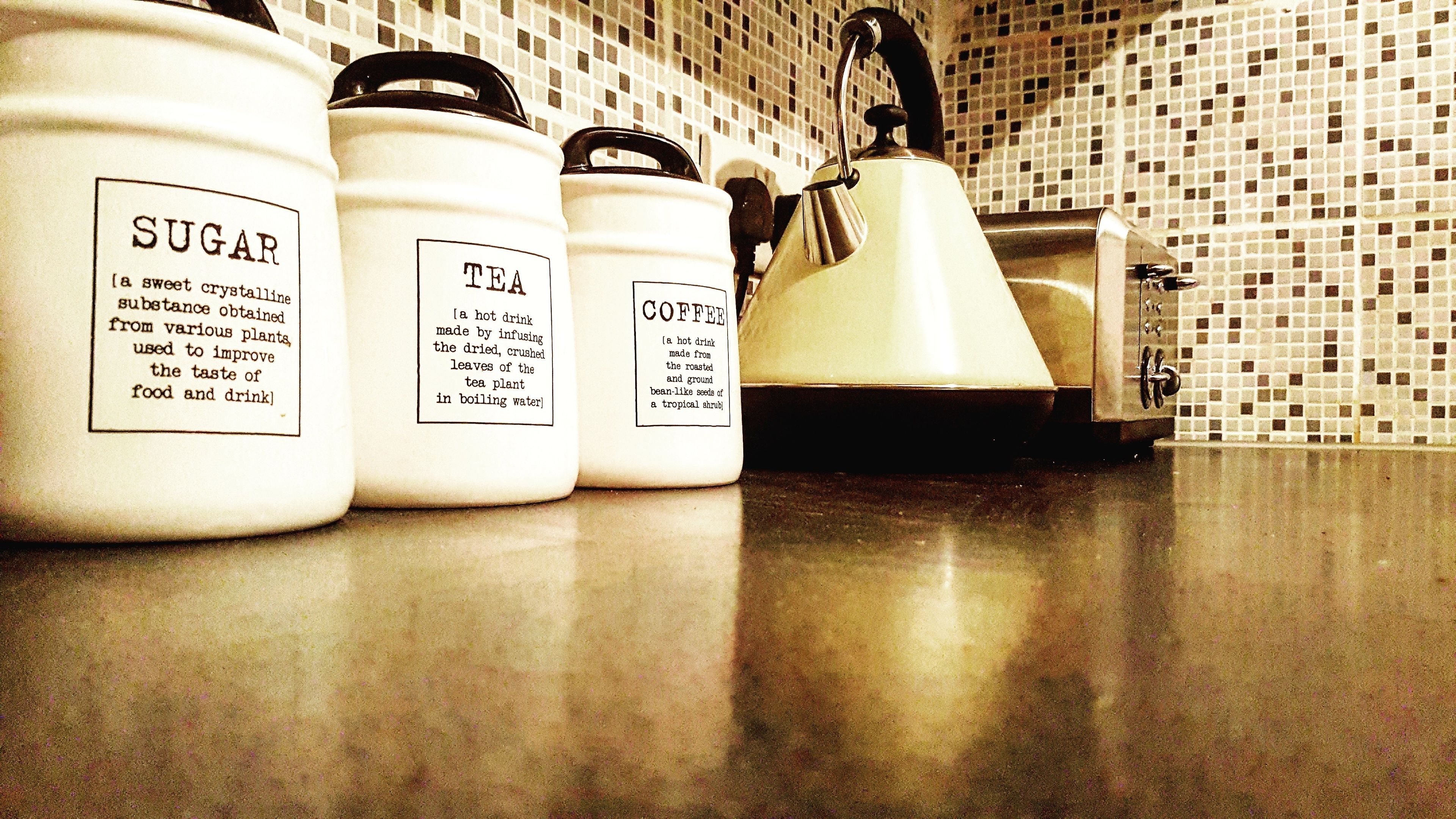 Three white containers labeled 'SUGAR,' 'TEA,' and 'COFFEE' on a kitchen counter.