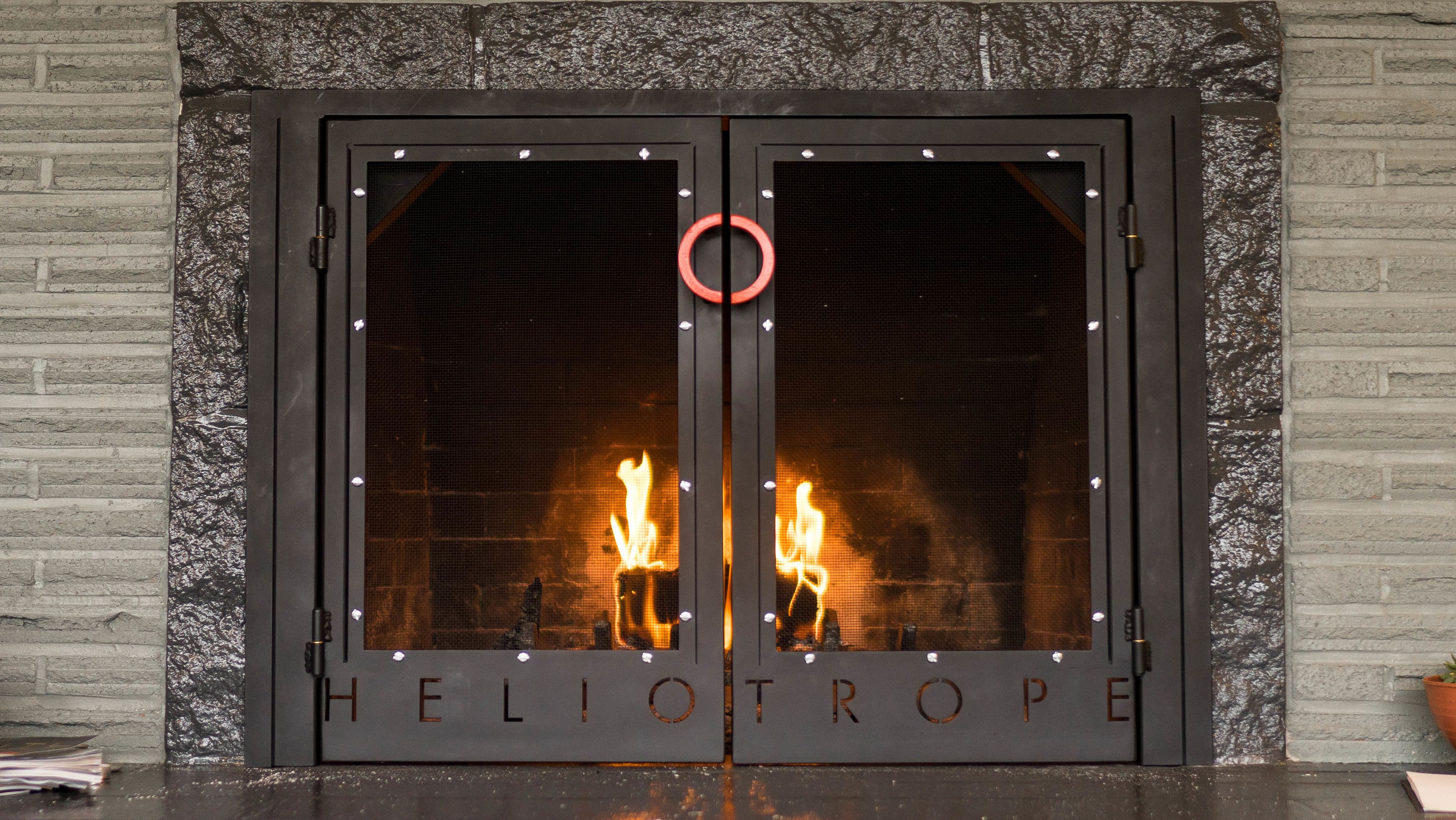 Unas dobles puertas con la palabra "HELIOTROPE" grabada, flanqueadas por dos velas encendidas.