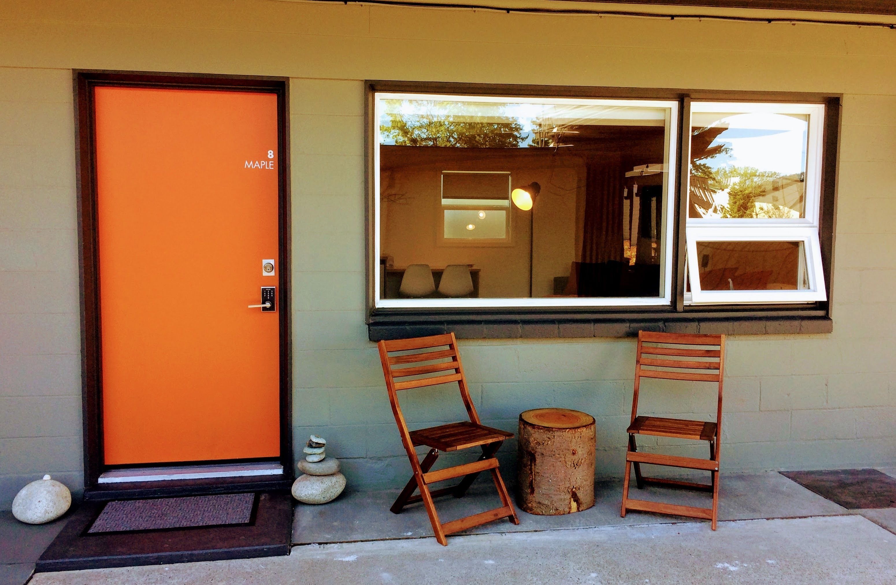 An orange door with the number 8 and the word "MAPLE" on it, two wooden chairs, a wooden stool, and a window with a view of the interior.