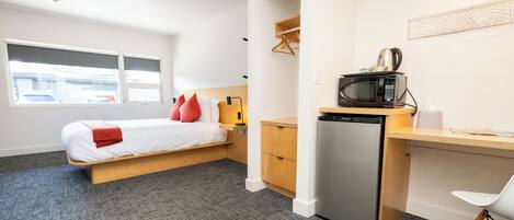 A compact hotel room with a bed, a desk, a microwave, and a refrigerator.