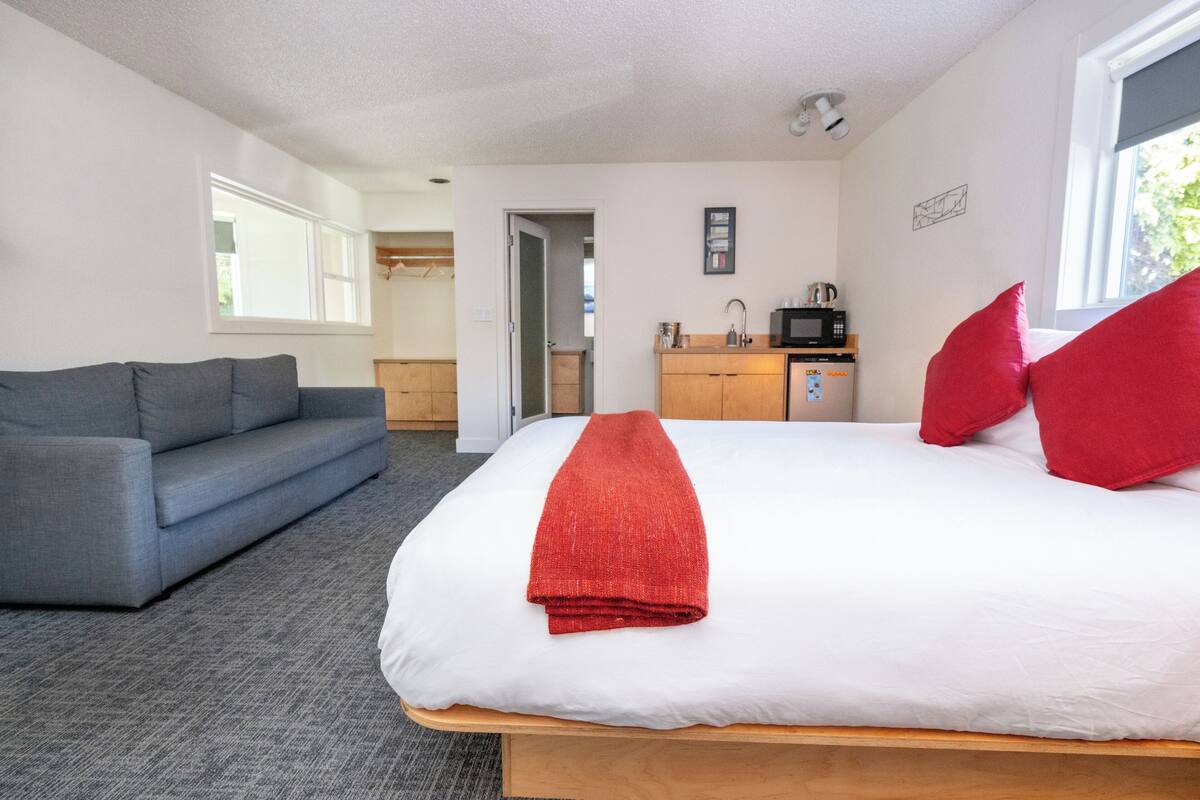 A hotel room with a bed, a grey sofa, a kitchenette, and a window.