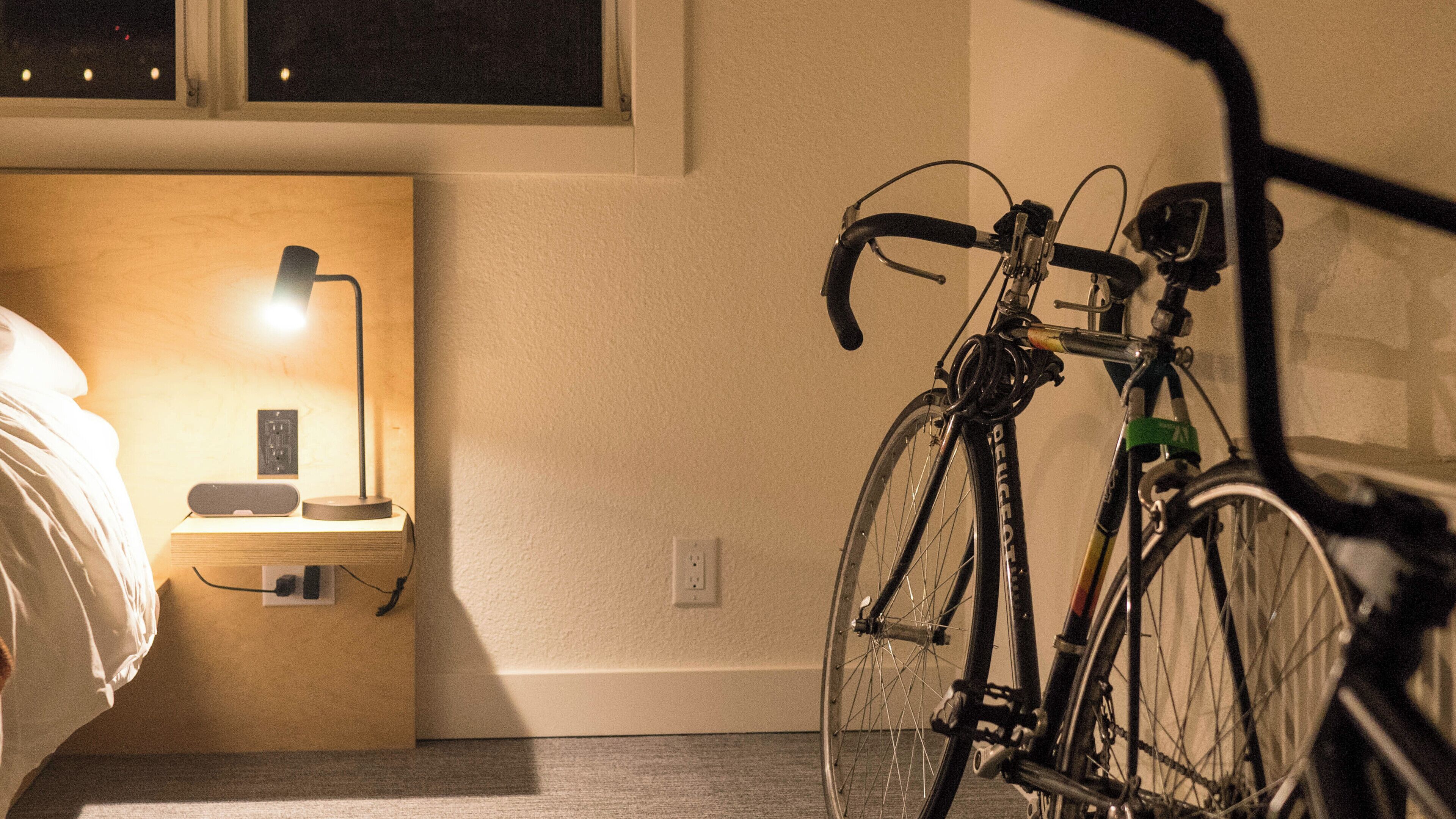 A bedroom with a bed, bedside table, lamp, and a bicycle leaning against the wall.