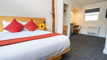Habitación de hotel con una cama grande, almohadones rojos, cabecera de madera, un escritorio y una silla.