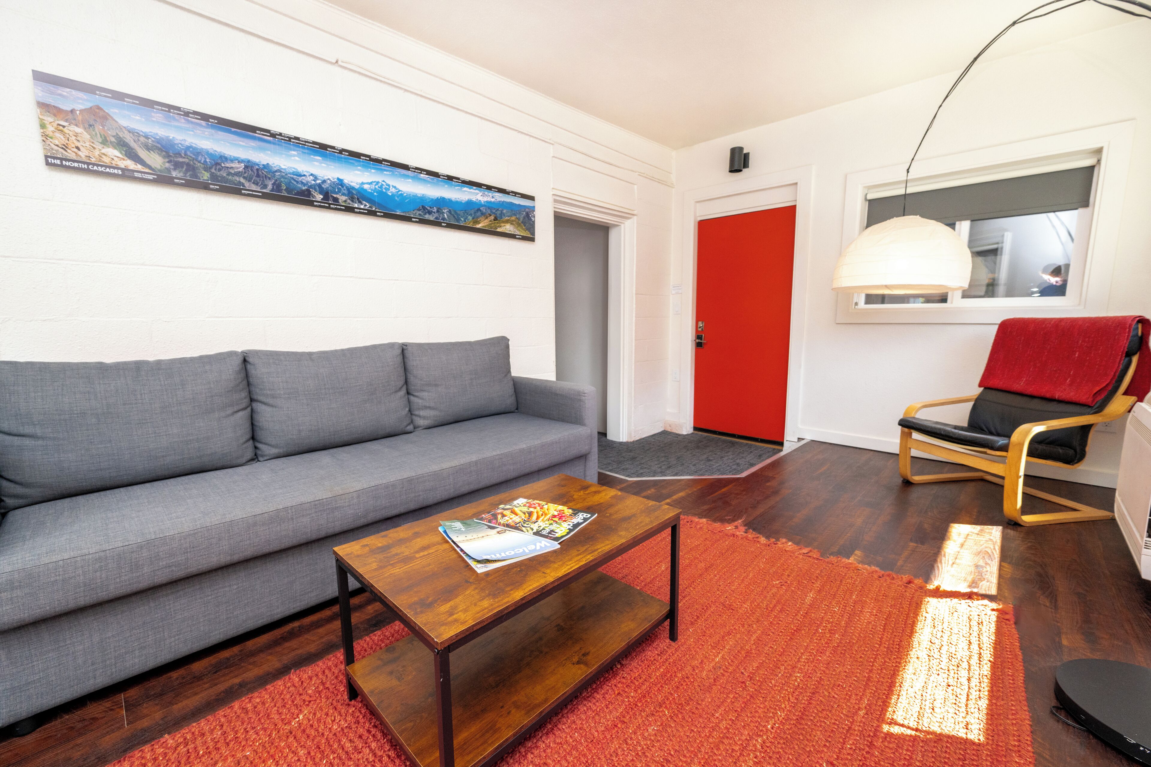A modern living room with a grey sofa, a wooden coffee table, and a red door.