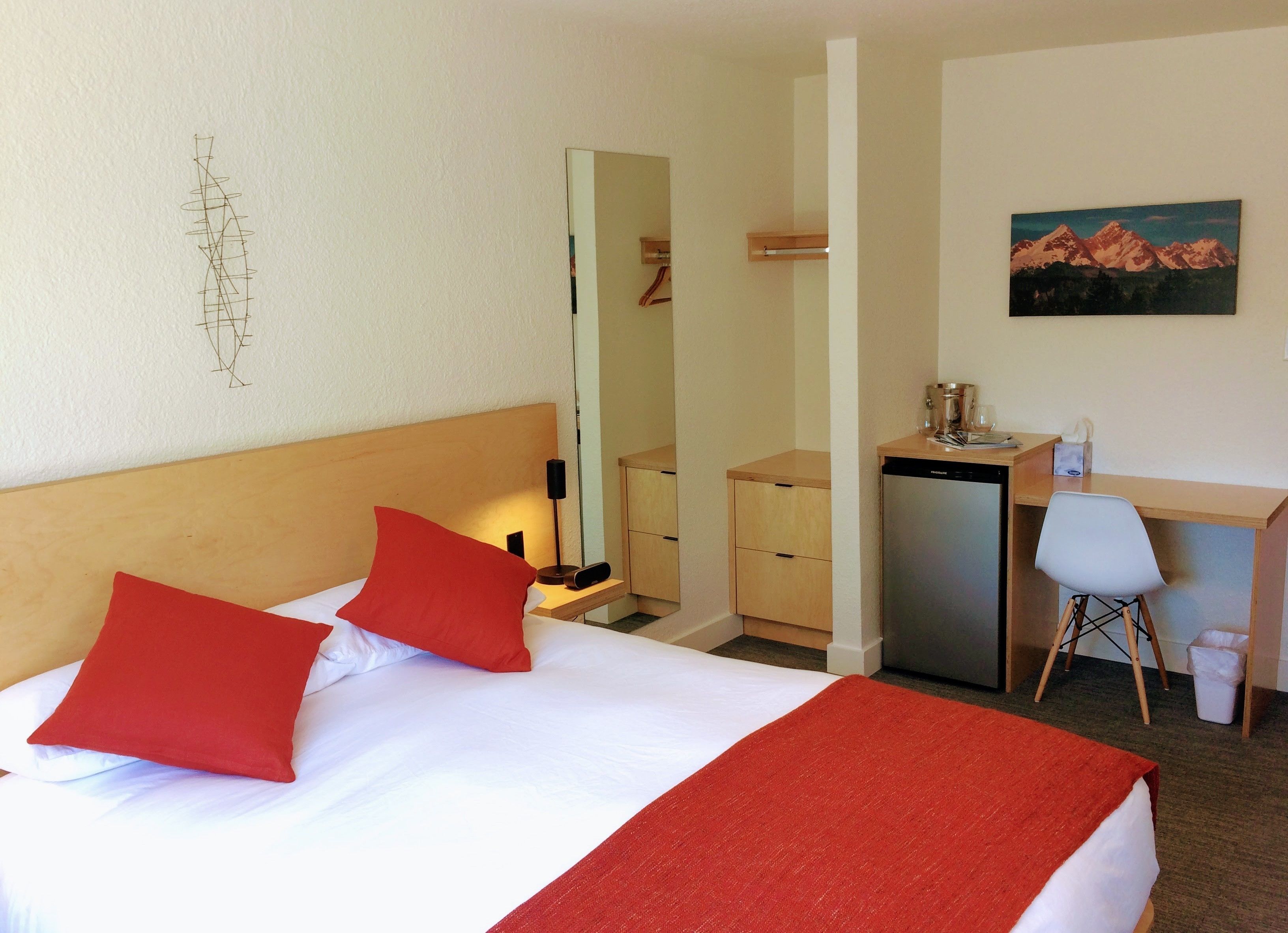 A hotel room with a bed, a desk, a chair, a mirror, and a painting on the wall.