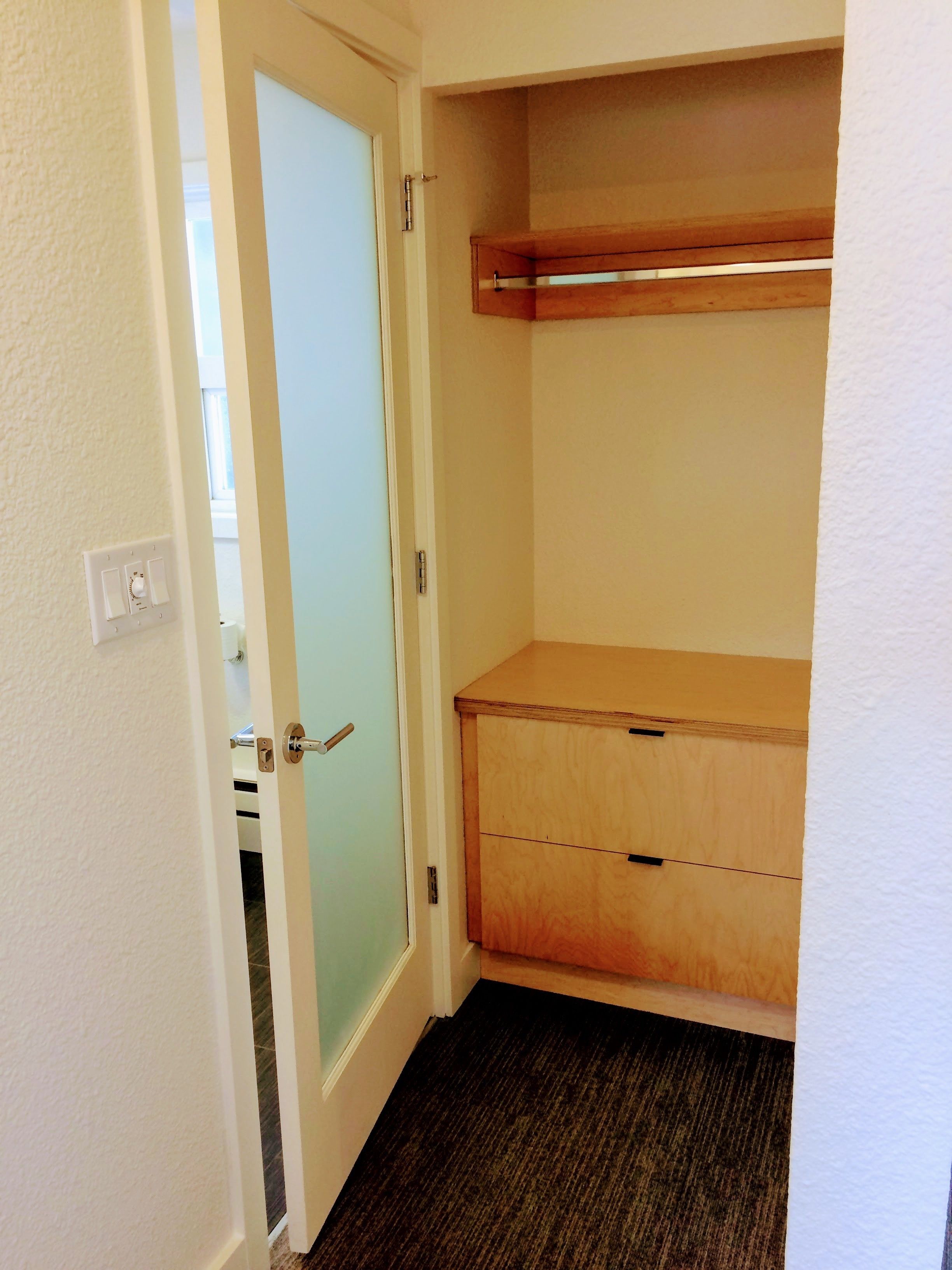 A walk-in closet with a wooden cabinet and a frosted glass door.