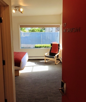 A hotel room with a bed, a chair, a window, and a door.