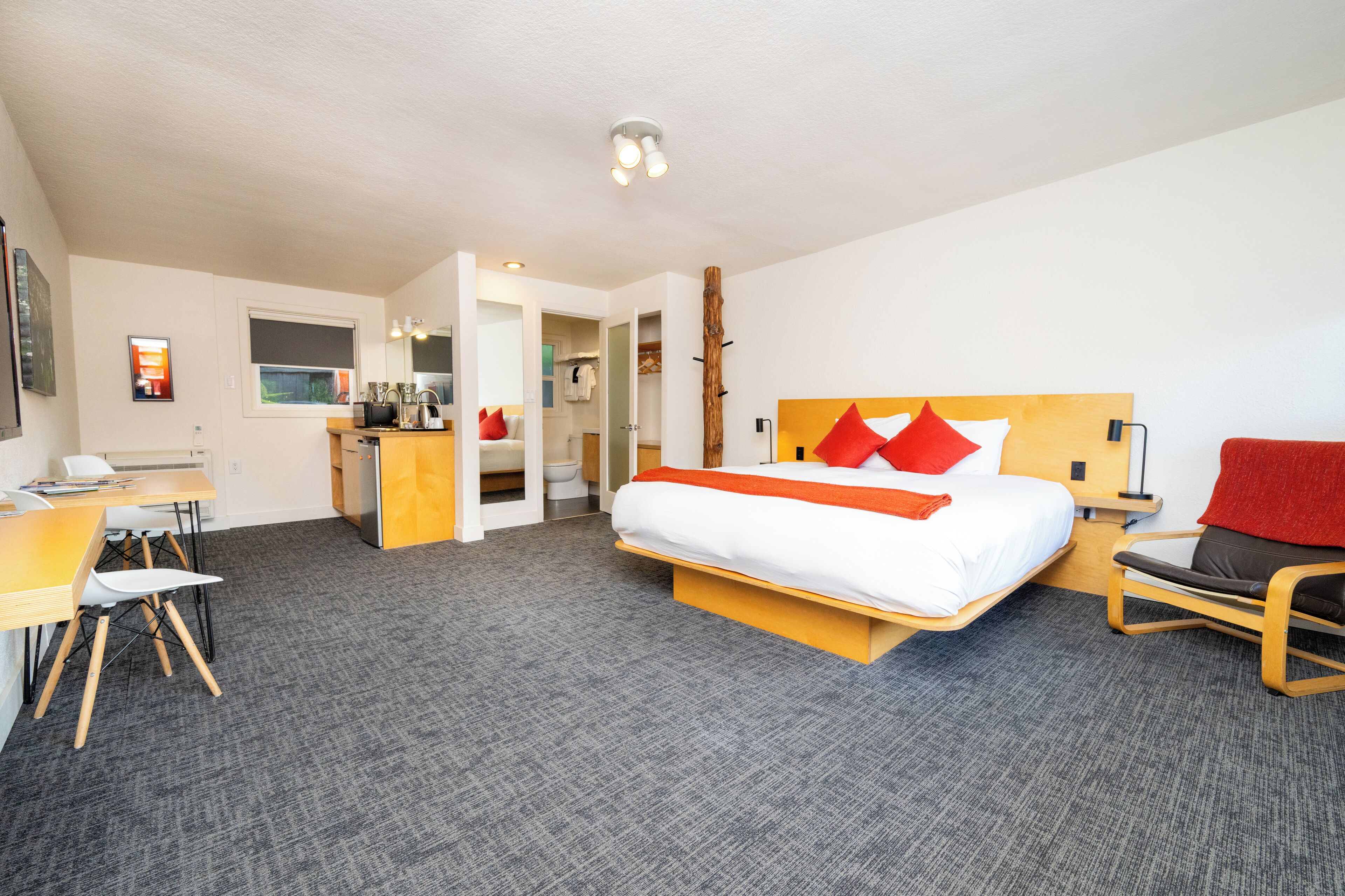 Una habitación de hotel con cama, escritorio, silla y una pequeña kitchenette.