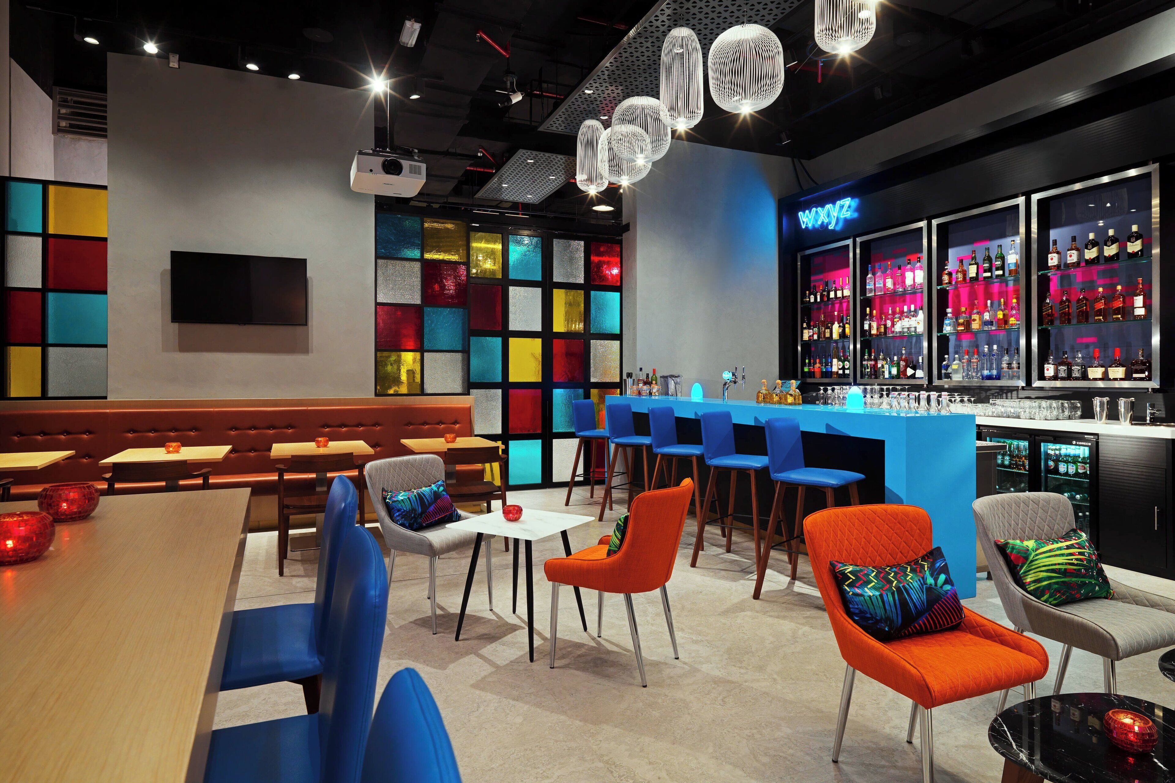 A modern bar area with a neon sign, colorful glass partitions, and a variety of seating options including tables and chairs.