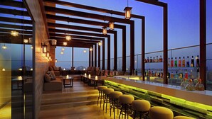 A rooftop bar with wooden beams, bar stools, and a variety of bottles. - Aloft by Marriott Palm Jumeirah (Dubai)
