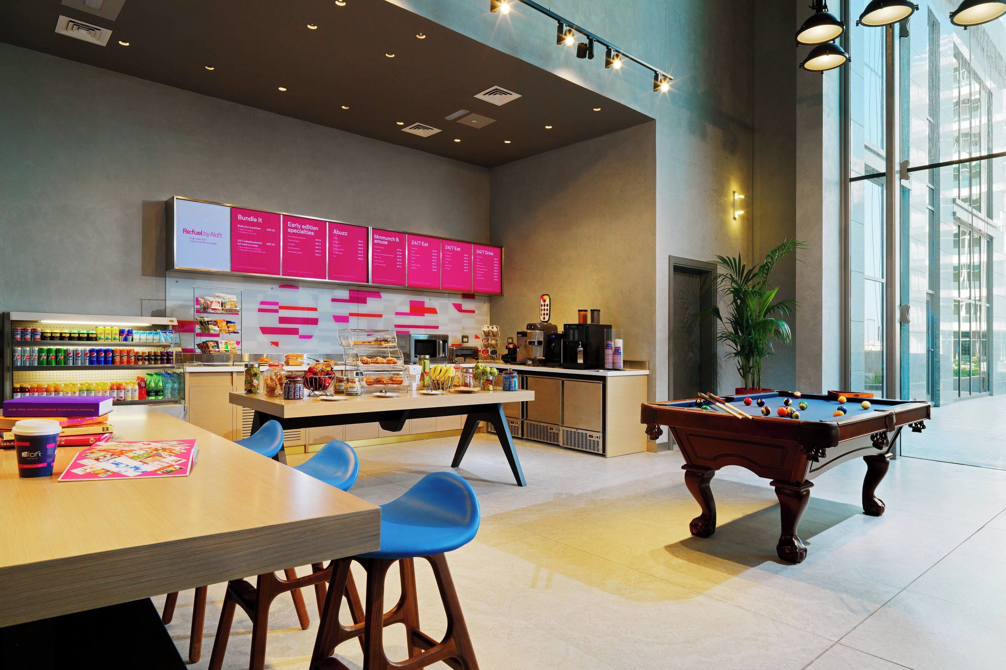 Espaço moderno em ambiente interno com mesa de bilhar, área de estar e bar com cardápio.
