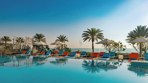 A poolside area with lounge chairs and umbrellas, palm trees, and a view of the coastline. - Aloft by Marriott Palm Jumeirah (Dubai)