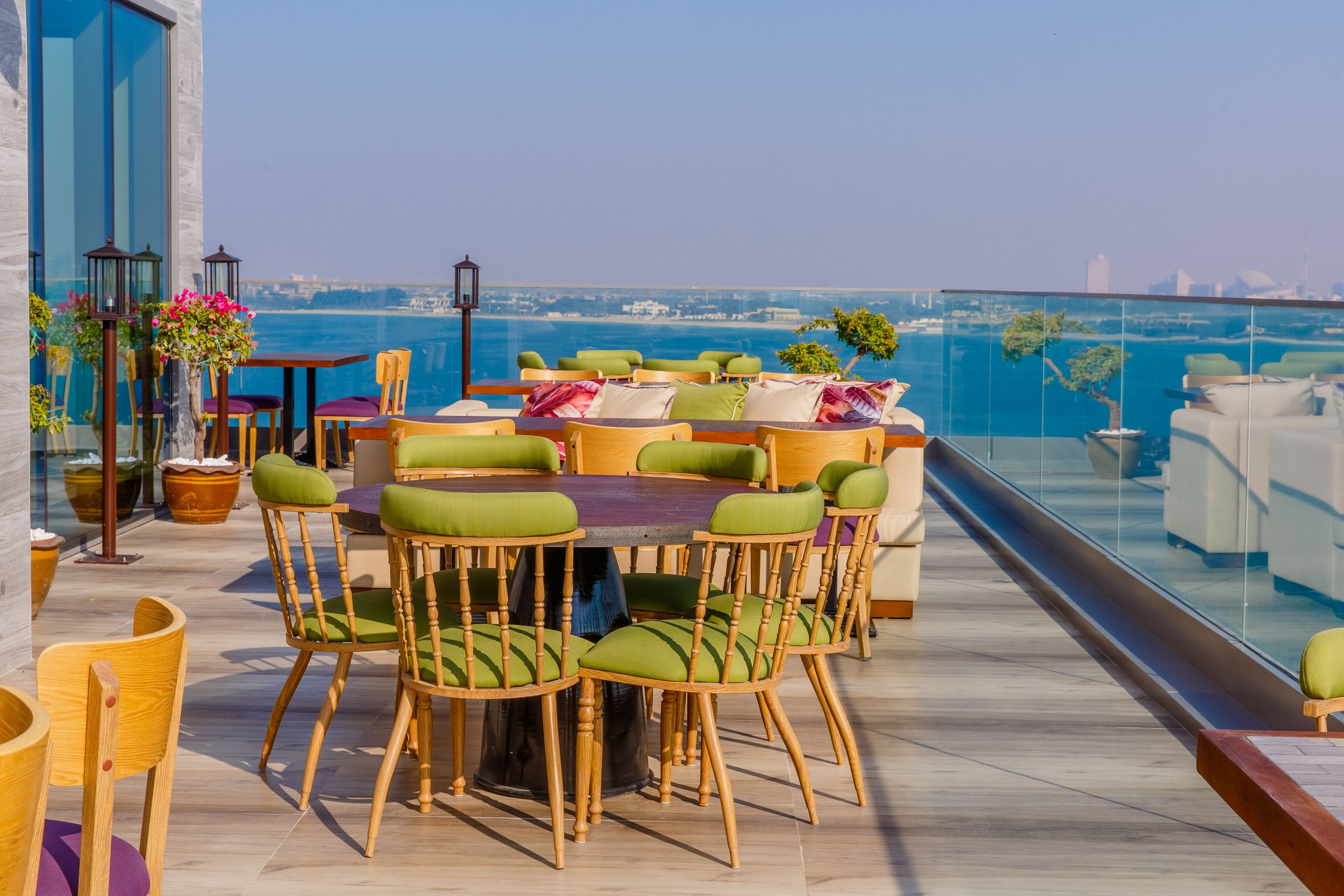 A rooftop terrace with a round table and chairs, overlooking a body of water and city skyline.