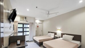 A hotel room with two beds, a desk, a TV mounted on the wall, and a ceiling fan.