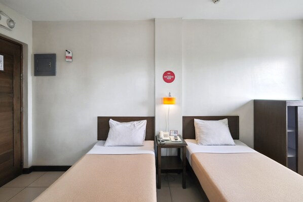 A hotel room with two single beds, a nightstand with a phone and lamp, a non-smoking sign, and a wooden wardrobe.