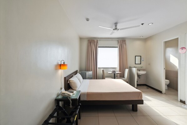 A hotel room with a bed, bedside table, lamp, and a view of the bathroom.