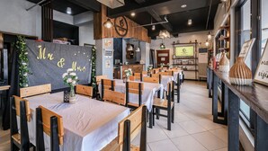 A restaurant interior with wooden tables and chairs, a chalkboard with 'Mr & Mrs' written on it, and a counter with a menu.