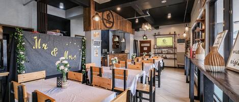 A restaurant interior with wooden tables and chairs, a chalkboard with 'Mr & Mrs' written on it, and a counter with a menu.