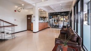 A modern hotel lobby with a reception desk, seating area, and a staircase.