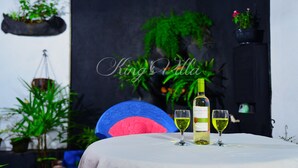 A table with a bottle of wine and two glasses, surrounded by potted plants and a blue chair. - Kings Villa (Matara)