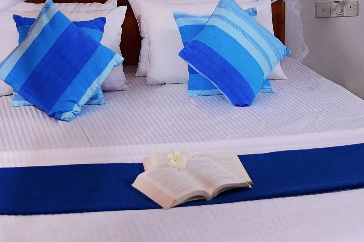 A bed with a striped bedspread, blue pillows, and a white flower.