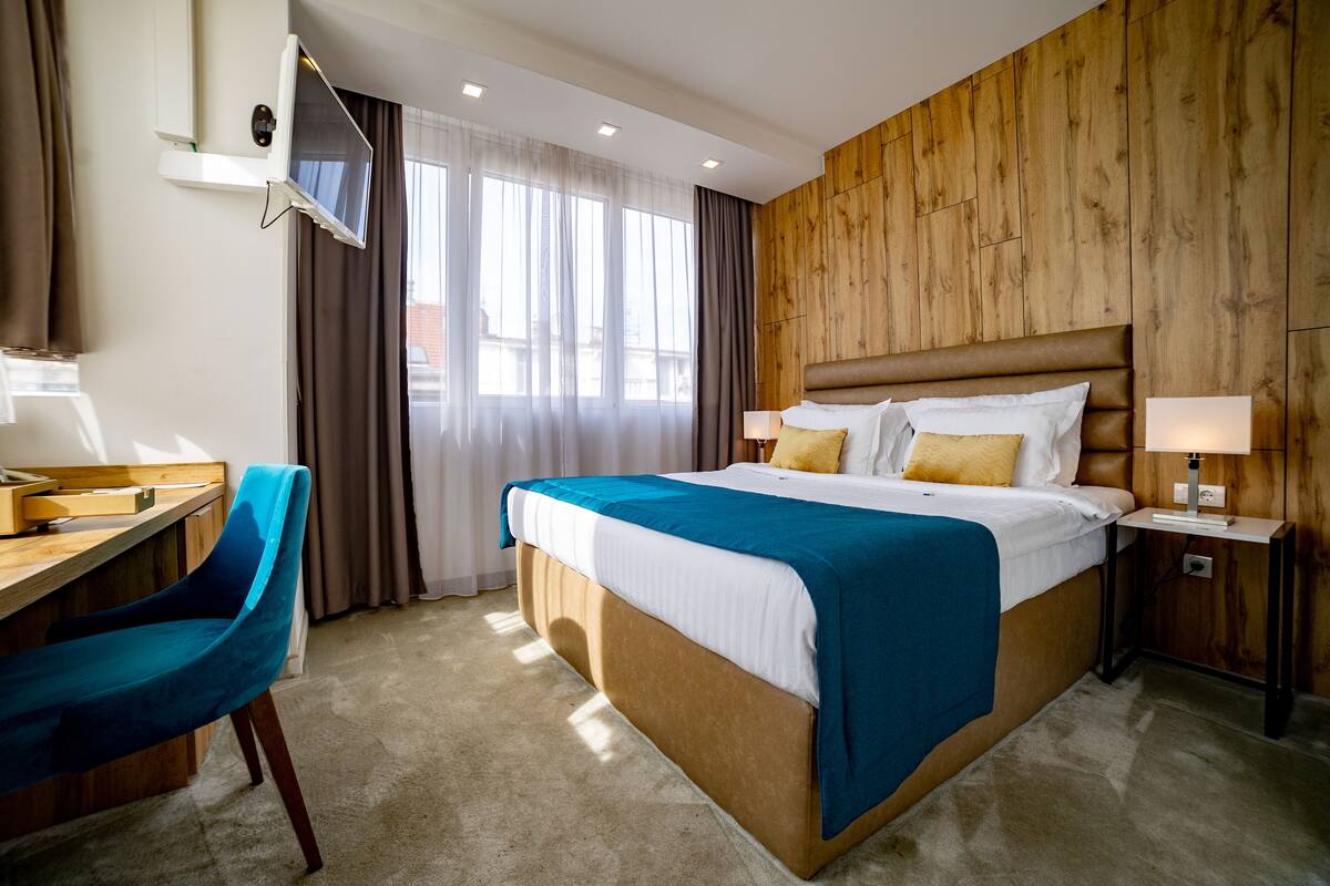 A hotel room with a bed, a desk, a chair, a TV, and a wooden wall.