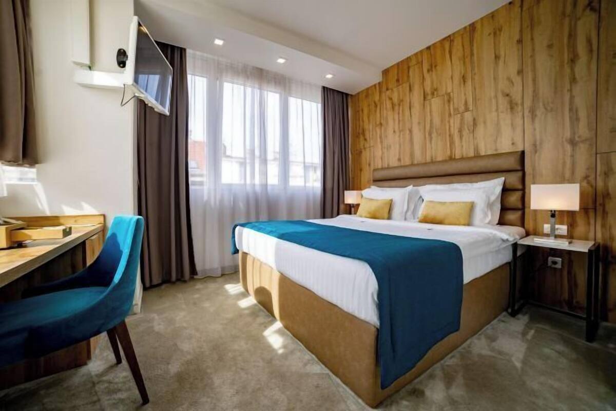 A hotel room with a bed, a desk, a chair, a TV, and curtains.