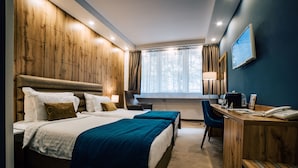 A hotel room with two beds, a desk, a chair, a TV, and a window with curtains.